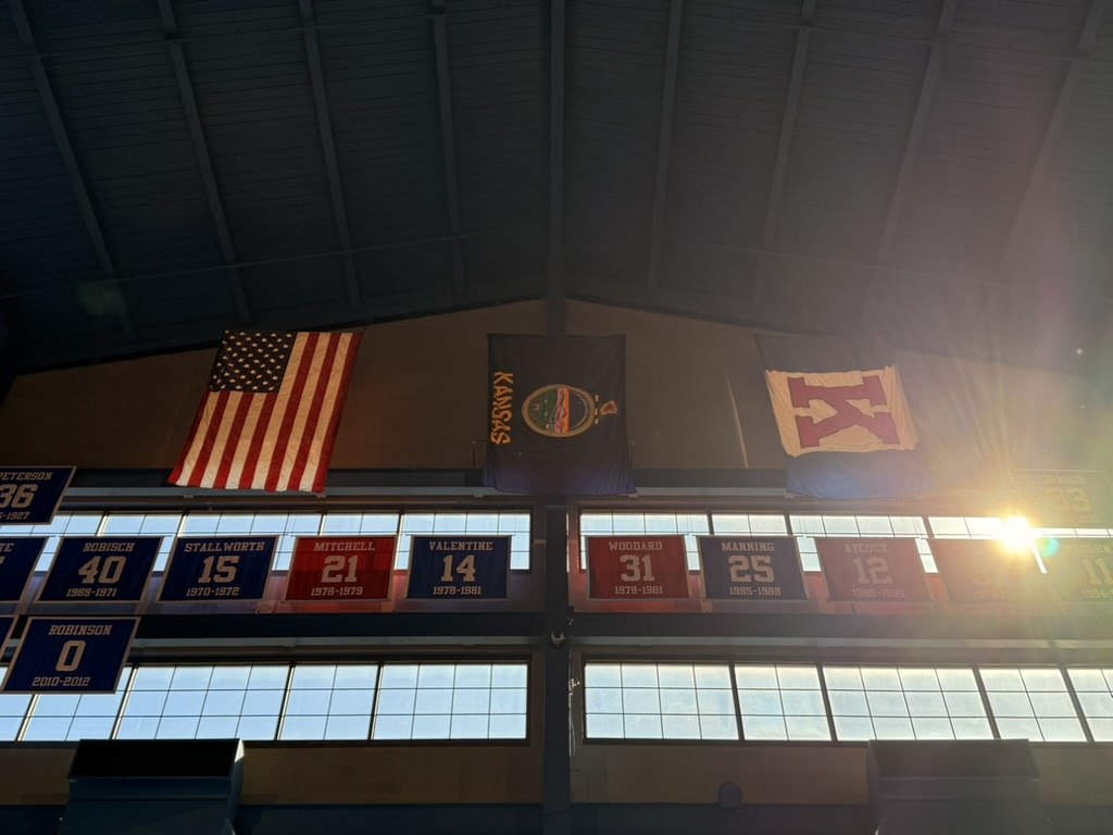 American, Kansas, and KU flags above retired jersey banners inside Allen Fieldhouse